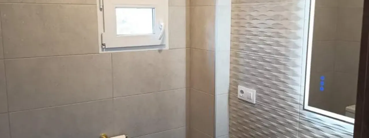 Baño con ducha, revestimiento claro y distribución compacta